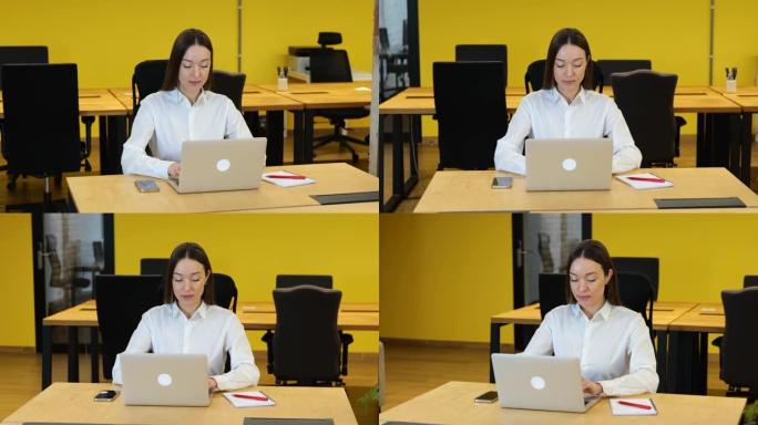 慢动作视频。白衬衫和灰色长裤的白人妇女正坐在她的工作台上，在她的电脑上工作，看起来非常热情和认真。