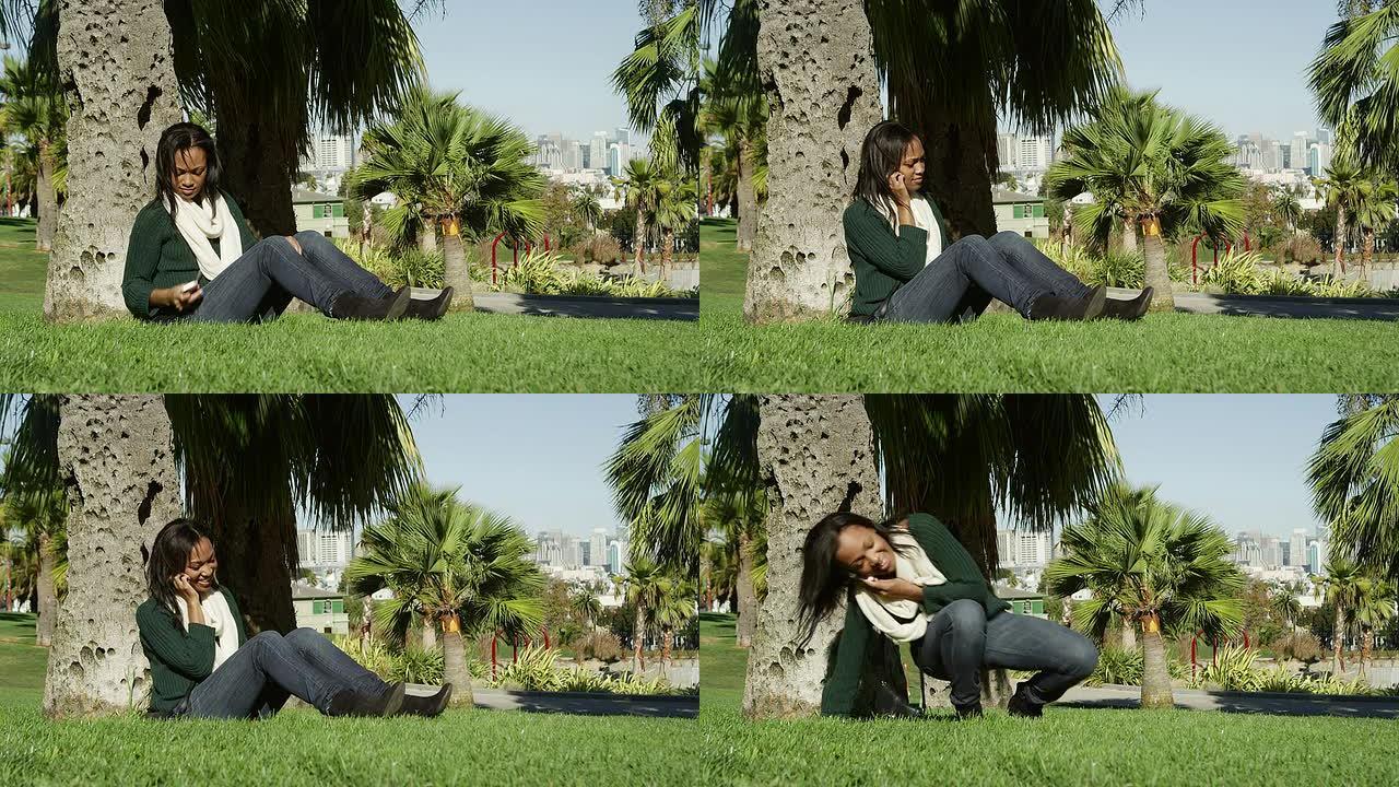 一位年轻女子白天坐在公园树下的草地上接听手机，然后起身离开