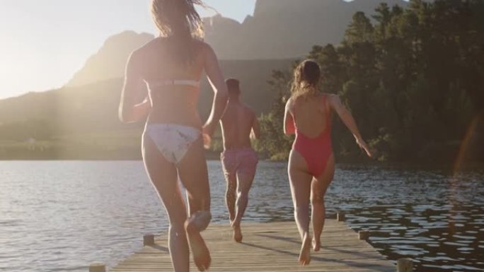 快乐的朋友在日落时从湖边的码头上跳下来，在水中嬉戏，享受自由分享夏季冒险
