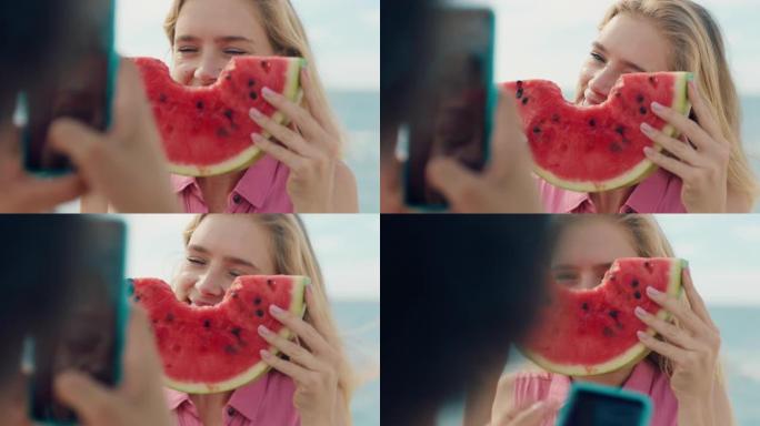 美丽的金发女人在海滩上吃西瓜为朋友拍照用智能手机女孩朋友在社交媒体上分享夏日在海边4k玩得开心