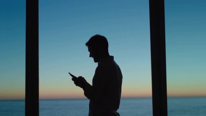 年轻人在酒店房间里使用智能手机发短信，在社交媒体上分享度假生活方式，享受日落时的海景