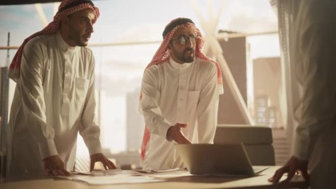 穿着白色传统服装的成功穆斯林商人举行办公会议，谈判和谈论金融机会。使用笔记本电脑。沙特、阿联酋、阿拉