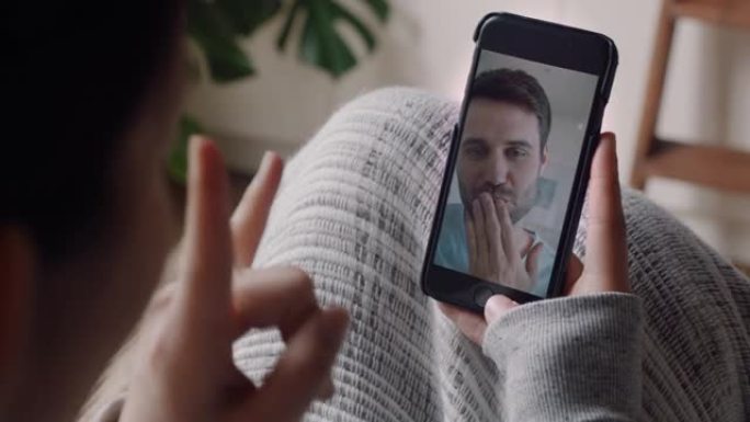 年轻女子在家中使用智能手机进行视频聊天，与男友吹吻，享受对话分享生活方式与手机交流