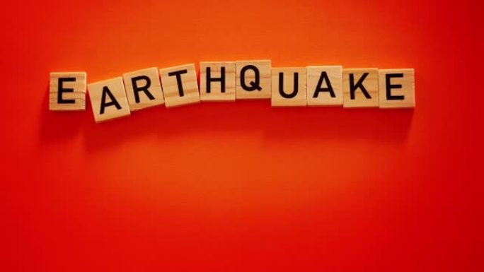 背景振动引起的铭文地震。地震、破坏和地壳移动的概念。带有字母的木制方形块放在橙色纸上。慢动作