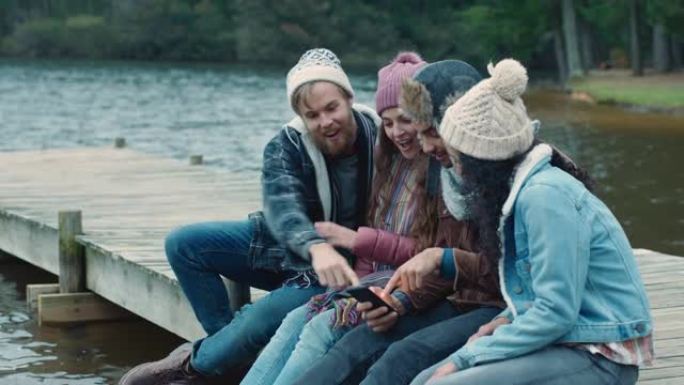 使用智能手机浏览照片的朋友一起分享回忆，坐在湖边的码头上聊天，在阴天的冬日穿着暖和的衣服闲逛