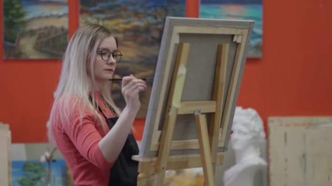 在工作室里，年轻的金发女子用丙烯酸颜料在画布上绘画，平移
