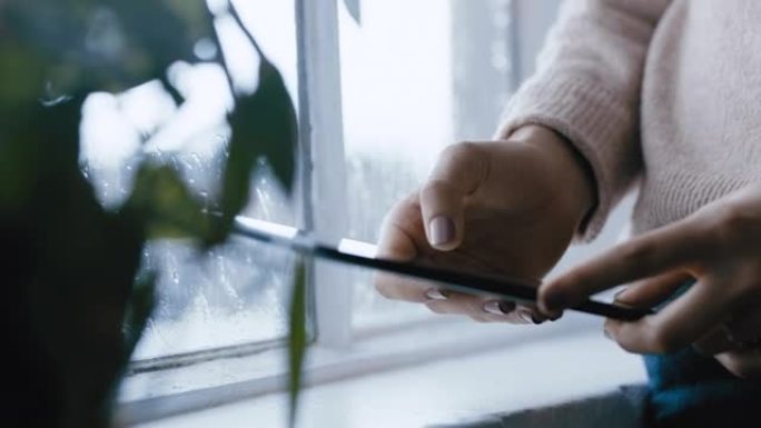 关闭女人的手使用数字平板电脑浏览在线消息阅读社交媒体享受移动触摸屏设备站在窗前放松在寒冷的雨天在家