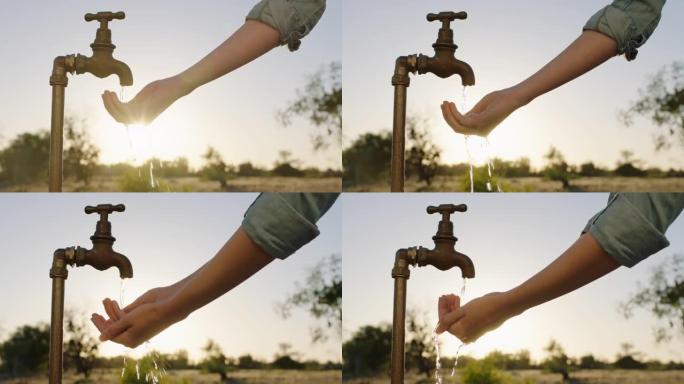女人的手在水龙头下取水口渴的农民在日落时饮用从水龙头流出的淡水节约用水概念