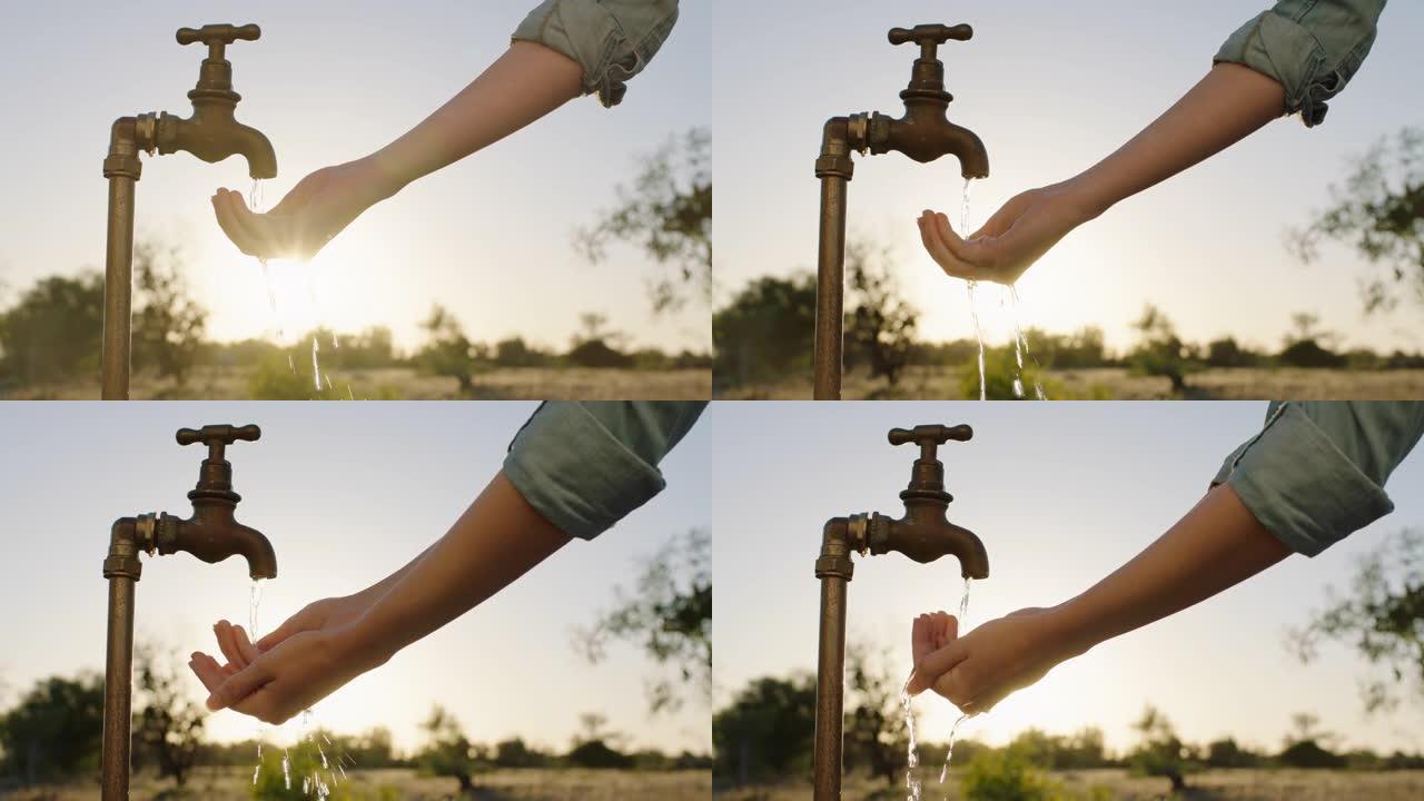 女人的手在水龙头下取水口渴的农民在日落时饮用从水龙头流出的淡水节约用水概念