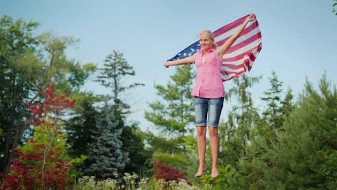 有魅力的女人与美国国旗在蹦床上跳在她的后院