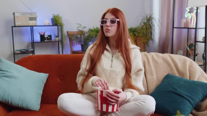 女人坐在沙发上吃爆米花，在家看有趣的3D电视电影，在线体育游戏