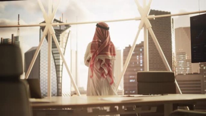 穿着传统白色服装的成功穆斯林商人走进他现代的办公室，看着窗外的摩天大楼。成功的沙特，阿联酋，阿拉伯商