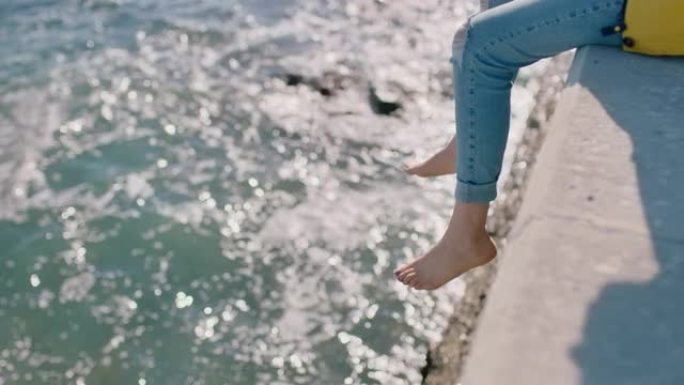 女人腿悬在水面上赤脚女孩享受暑假坐在海边码头看海浪自由概念