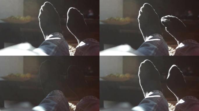 小男孩休息一下，在电视前用被太阳照亮的袜子玩脚