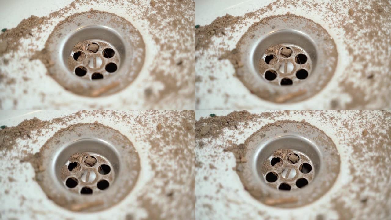 沙子上白色盥洗台的排水孔，特写。肮脏的白色陶瓷水槽