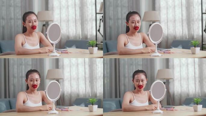 美丽的年轻亚洲女子坐在镜子前，使用胶原蛋白唇膜干燥干裂的嘴唇，并在家里照顾皮肤时对着镜头微笑
