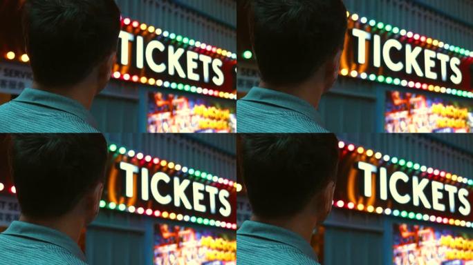 快乐的男人欣赏游乐园入口处五颜六色的嘉年华门票摊位标志