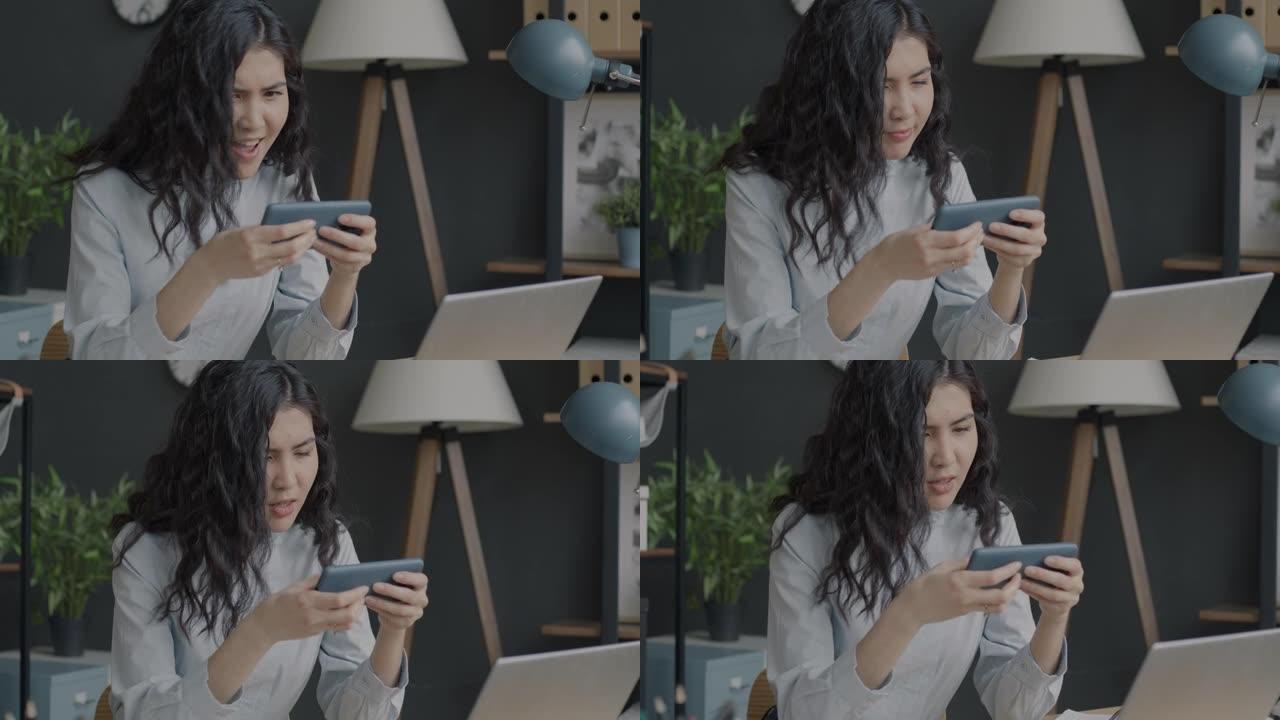 无忧无虑的亚洲女士玩手机视频游戏，在办公室享受娱乐