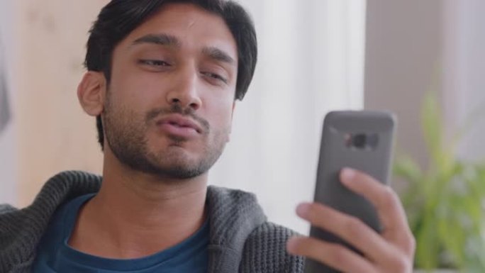 快乐的印度男子使用智能手机进行视频聊天，挥舞着婴儿吹吻，享受在家中的手机聊天