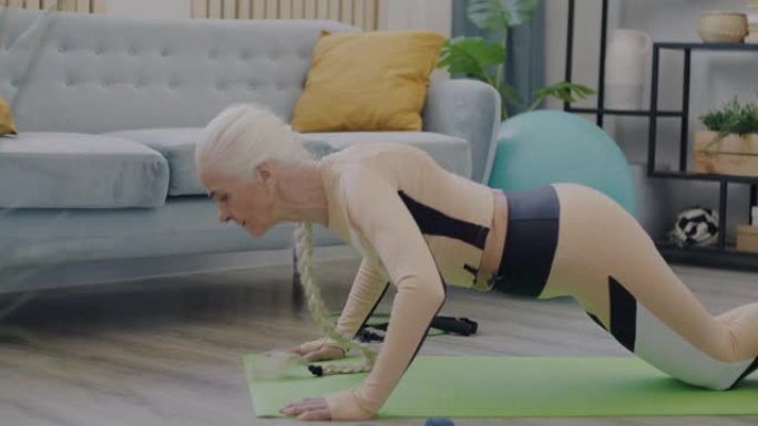 穿着运动服做俯卧撑的老年女士的侧视图集中在家里进行体育锻炼
