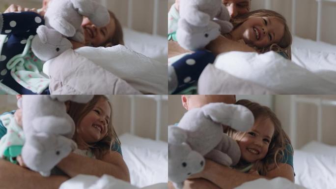 快乐的父亲在床上拥抱女儿小女孩笑着享受爸爸的拥抱