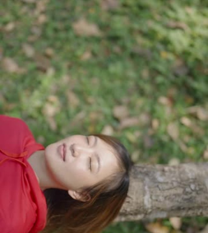 亚洲妇女躺在绿草地上的树干上休息