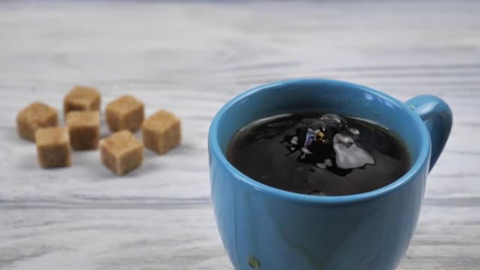 一立方红糖以慢动作，特写镜头落入白色木制背景上的红茶杯子中。早晨热能量饮料，红甜茶，早餐，配料概念