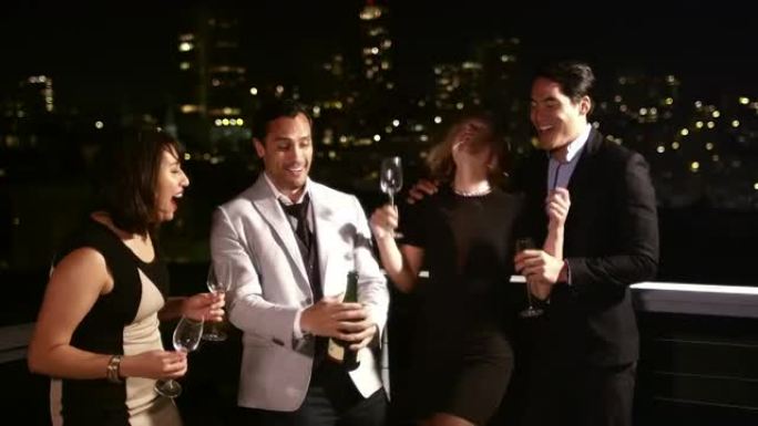 一群朋友晚上站在屋顶上，打开一瓶香槟庆祝