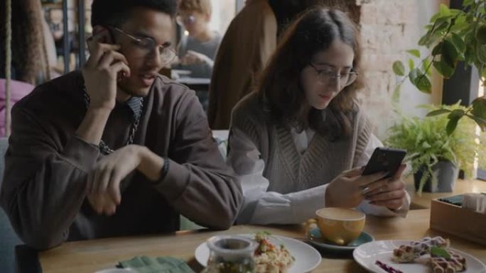 年轻人在手机上聊天的肖像，而女友一起坐在咖啡馆的桌子上使用智能手机