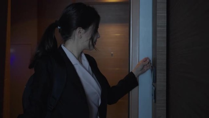 女商人打开酒店房间的门，插入感应卡以打开照明和空调系统。