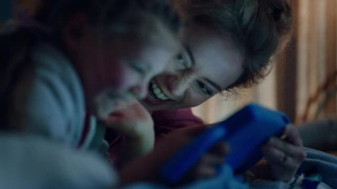 母亲和孩子使用平板电脑妈妈教小女孩在触摸屏技术上玩游戏睡前玩得开心