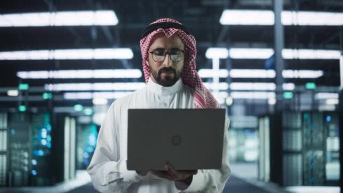 穆斯林数据中心技术经理的肖像穿着传统的白色衣服，在现代技术服务器农场设施中使用笔记本电脑。工作中的阿