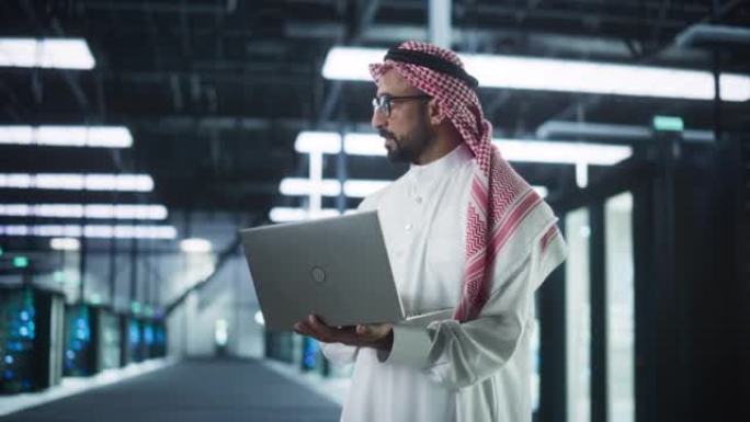 中东IT系统工程师的肖像穿着传统的白色长袍，在现代技术服务器农场设施中使用笔记本电脑。工作中的阿拉伯