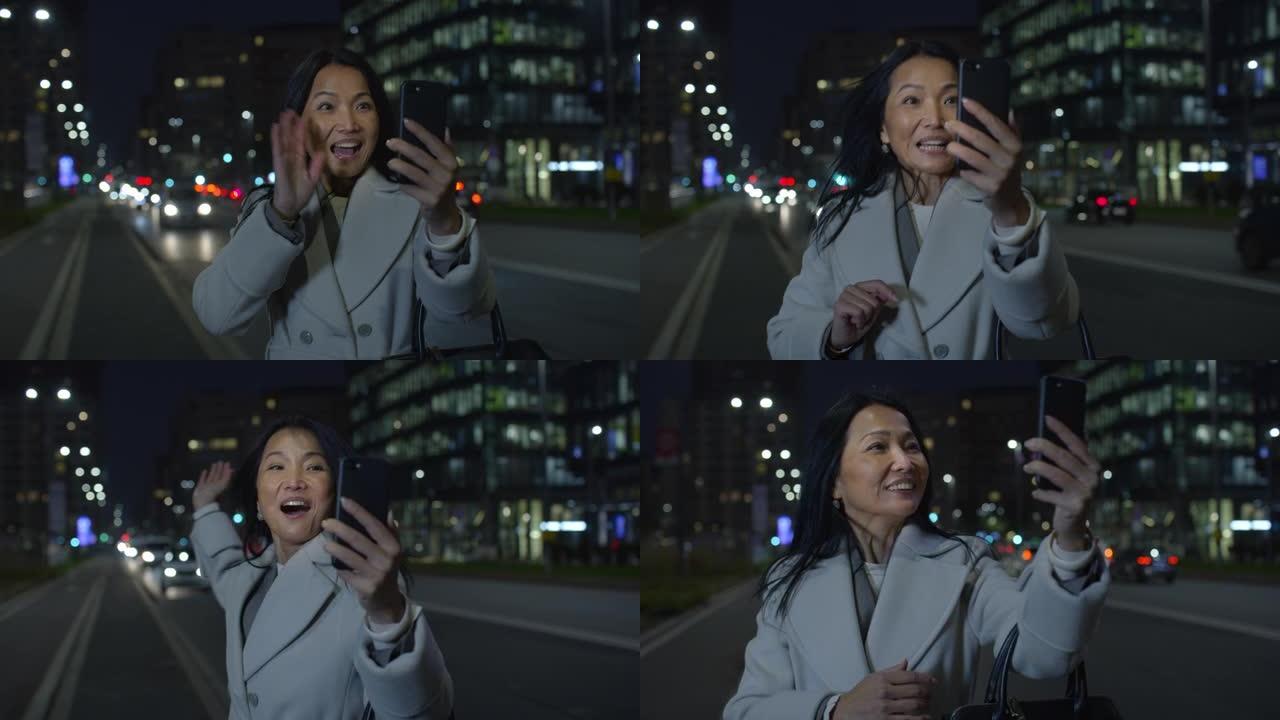 真实的亚洲中年女商人的肖像，晚上在城市街道上使用智能手机进行视频通话。出差中的女CEO，在网上与家人