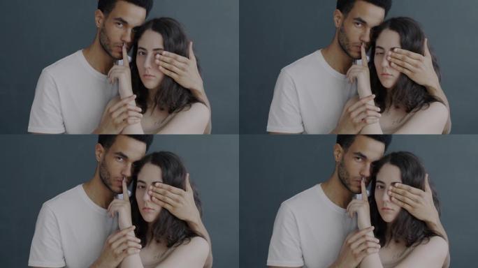 男人和女人的慢动作肖像遮住眼睛，用手指触摸嘴巴站在灰色背景上，表情严肃