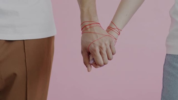 男性和女性的双手包裹着红色的绳子，在粉红色的背景下触摸握持