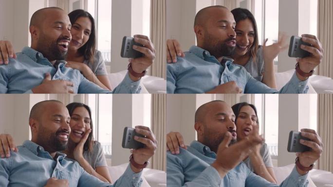 快乐的混血夫妇使用智能手机视频聊天与朋友微笑兴奋享受在线交流吹吻挥手告别