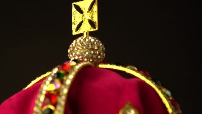 仪式加冕钻石皇冠顶部的极端宏观特写由金色和红色皇家软天鹅绒材料制成。黑色背景。慢速旋转运动。4k，u