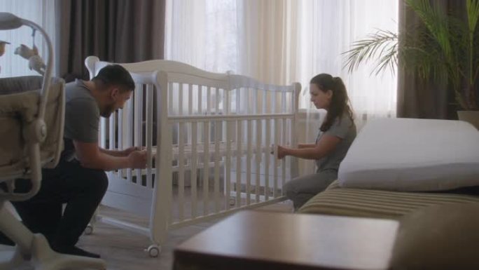 父母在托儿所为未来的婴儿组装白色婴儿床