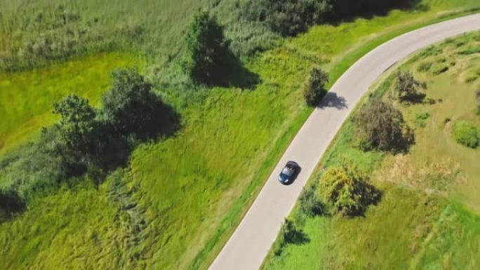 一辆现代汽车在蓝天湖边绿色田野的道路上行驶的鸟瞰图