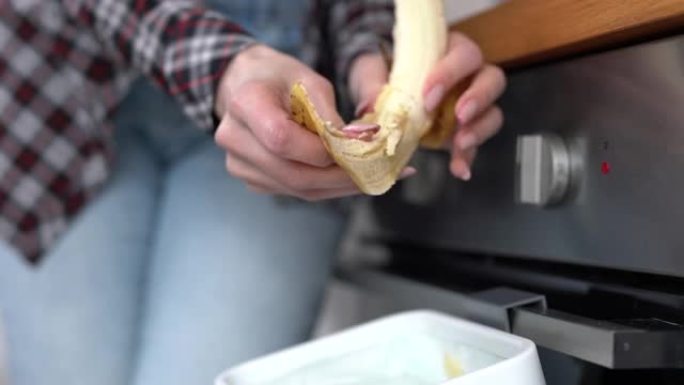 女人把香蕉皮扔进堆肥箱。女性在家庭厨房的bokashi容器中回收有机食物垃圾