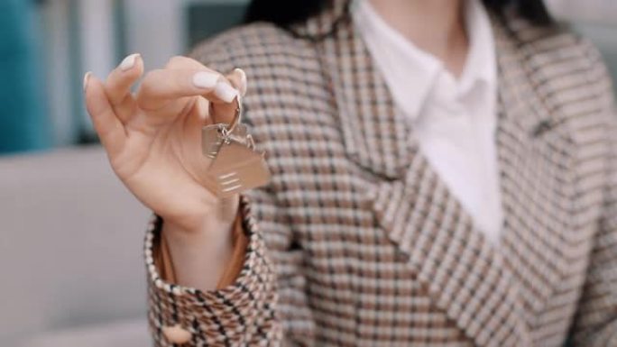 特写焦点女性手握着向相机展示一串带家庭形状钥匙扣的钥匙。新家，租赁