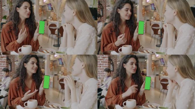 快乐的朋友看着色度键绿屏的智能手机，在咖啡馆室内聊天