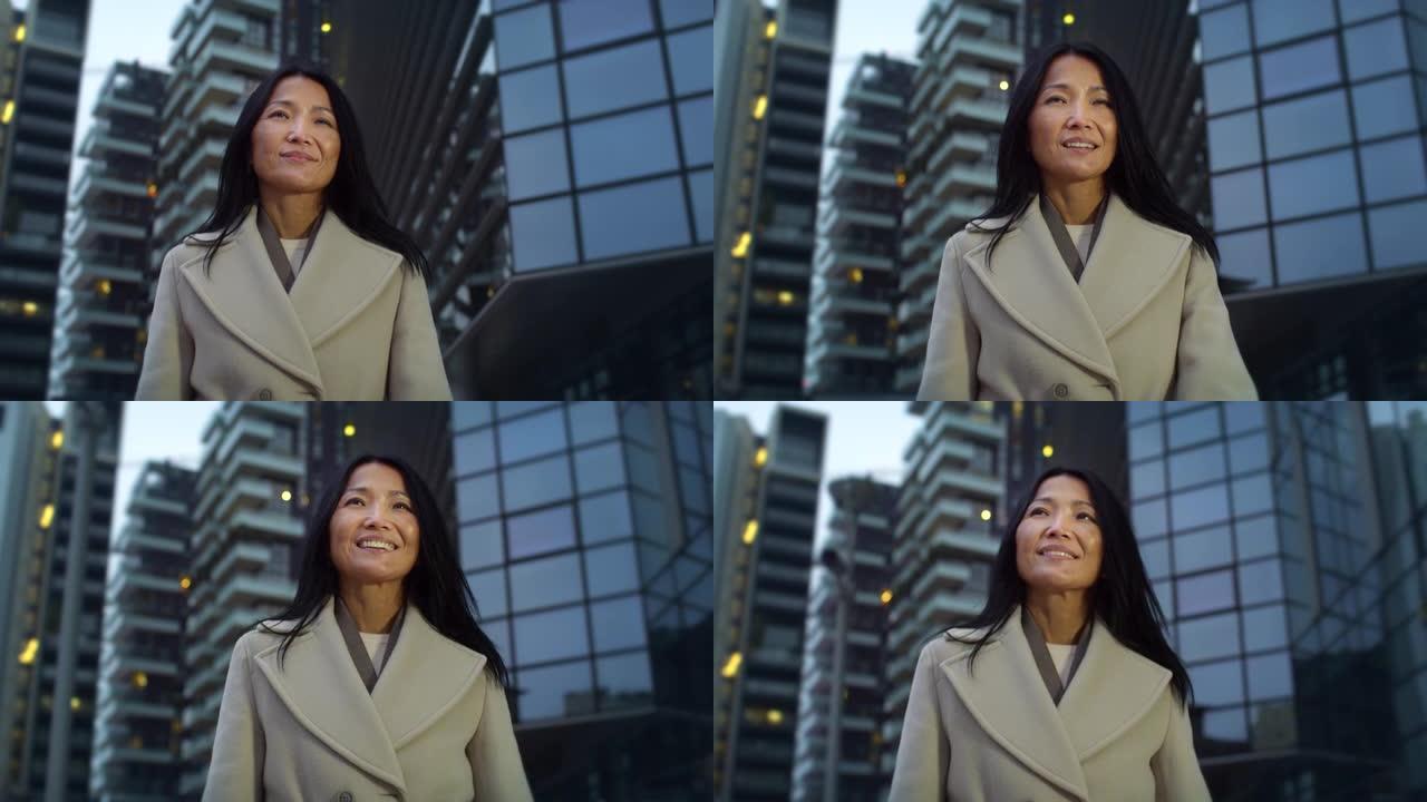 真实的中年亚洲女商人在早晨走向办公室的低角度肖像。快乐的成功女律师微笑着走在街上。自信的女人准备好工