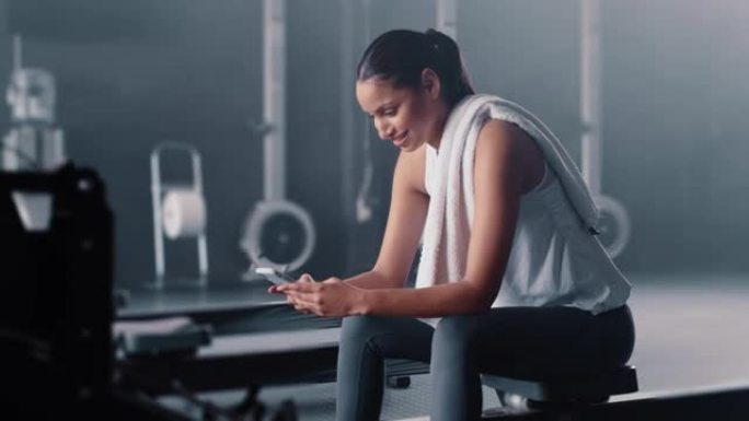 智能手机，女人和在健身房休息，微笑和社交媒体的锻炼，健康进步或短信应用程序。快乐女性，运动休息和移动