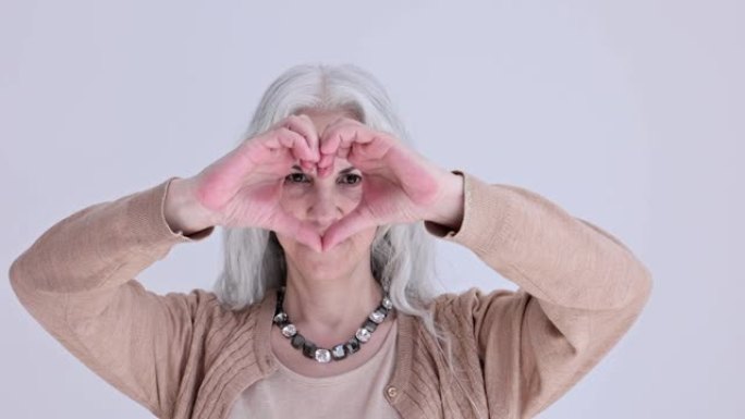 积极成熟的女人在光工作室用手掌显示心脏