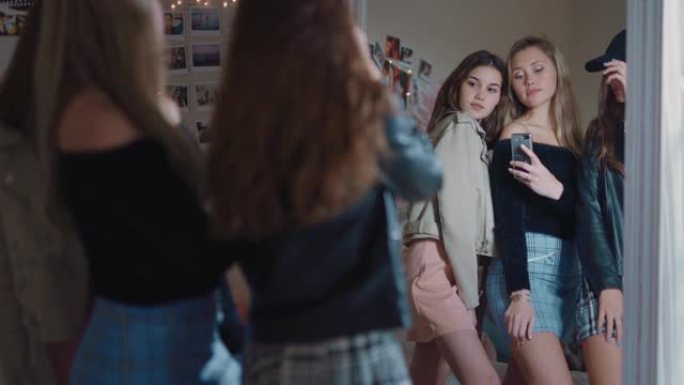 快乐的女孩朋友使用智能手机在镜子里摆姿势拍照，在社交媒体上分享时尚的时尚，享受周末在家一起出去玩