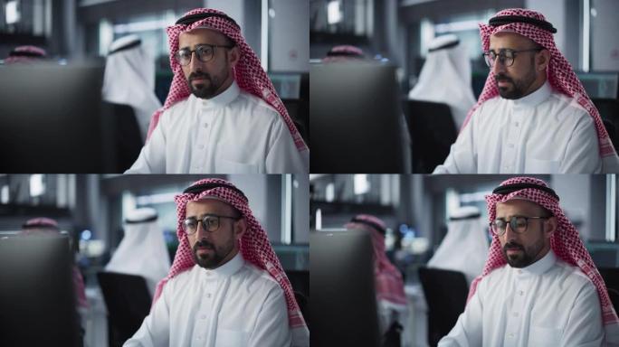 在技术初创公司服务台部门工作的聪明的年轻阿拉伯专家的肖像，在多元化的办公室中使用计算机。男性穿着传统