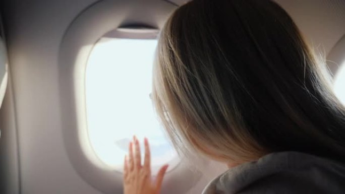 一个女人打开舷窗窗帘，看着飞机的窗户。