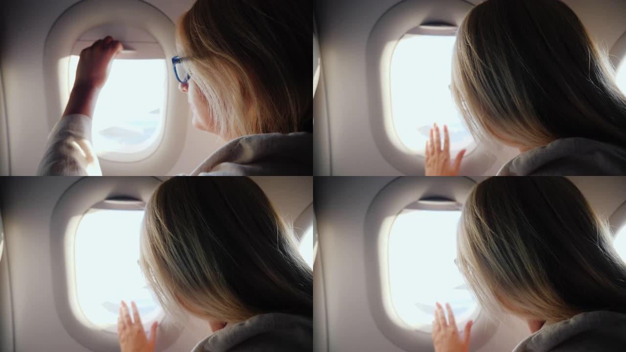 一个女人打开舷窗窗帘，看着飞机的窗户。